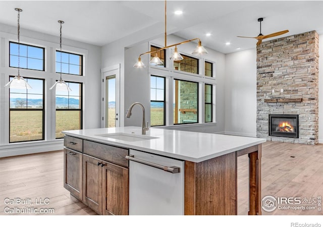 1233 Eliza Ave, Berthoud, CO 80513 - kitchen featuring dishwasher, ceiling fan, light wood-style flooring, hanging light fixtures, and a stone fireplace