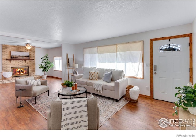 living room with ceiling fan, hardwood / wood-style flooring, a fireplace, and a textured ceiling