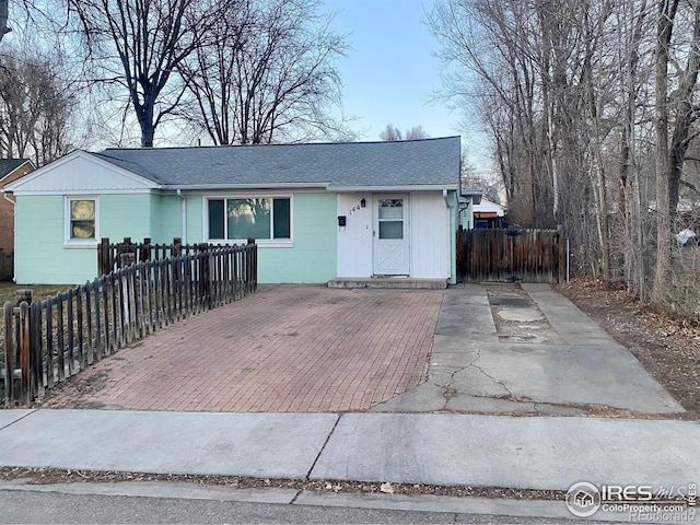 ranch-style home with roof with shingles, a fenced front yard, and concrete block siding