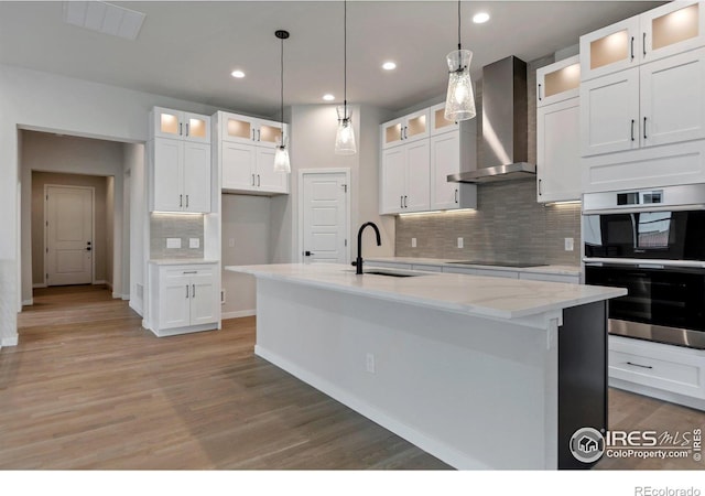 kitchen featuring an island with sink, wall chimney exhaust hood, sink, and white cabinets