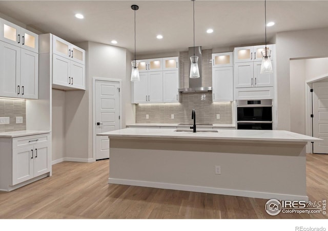 kitchen with white cabinetry, pendant lighting, an island with sink, and wall chimney exhaust hood