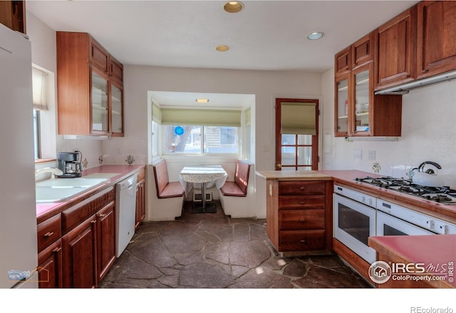 kitchen featuring glass insert cabinets, light countertops, white appliances, and stone finish flooring