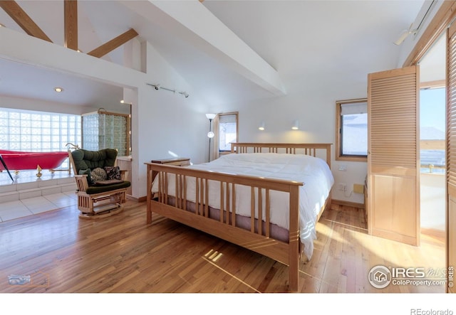bedroom with beamed ceiling, baseboards, light wood finished floors, and high vaulted ceiling
