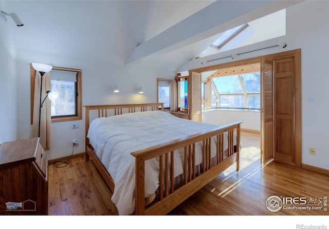 bedroom with baseboards, lofted ceiling with skylight, and light wood finished floors