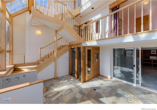 unfurnished living room featuring baseboards, a high ceiling, stone floors, and stairway