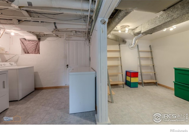 basement featuring washing machine and dryer, baseboards, refrigerator, and light tile patterned floors
