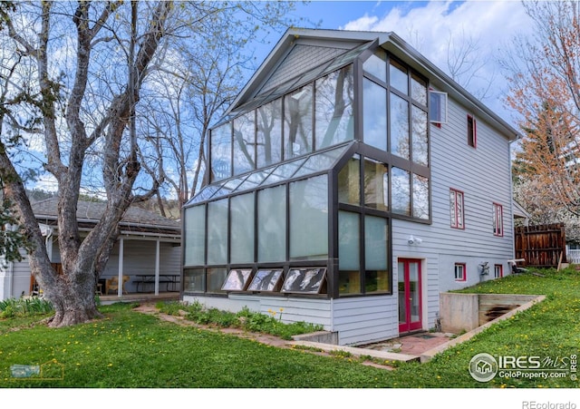 rear view of property featuring a sunroom, fence, and a lawn