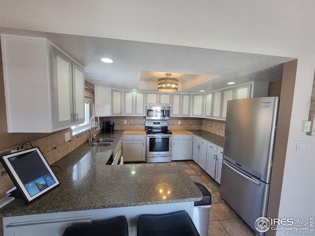 kitchen with appliances with stainless steel finishes, a breakfast bar, sink, white cabinets, and kitchen peninsula