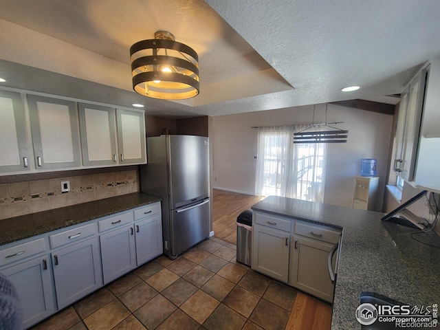 kitchen featuring pendant lighting, stainless steel fridge, backsplash, a tray ceiling, and a textured ceiling