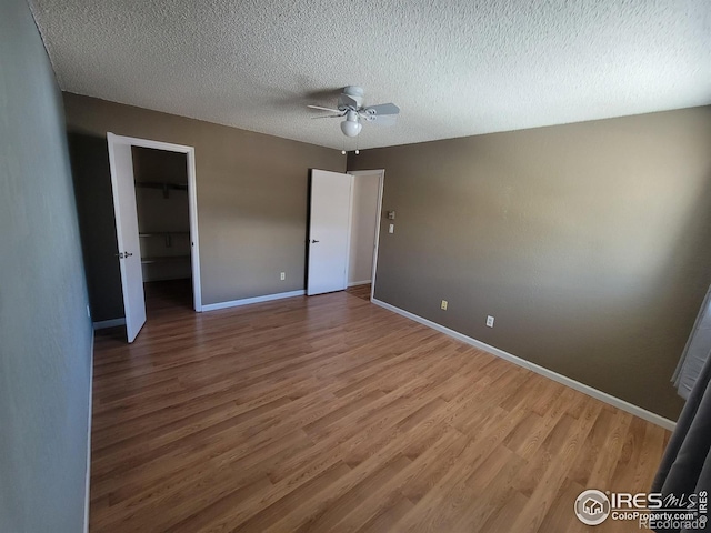 unfurnished bedroom featuring a spacious closet, a textured ceiling, a closet, hardwood / wood-style flooring, and ceiling fan