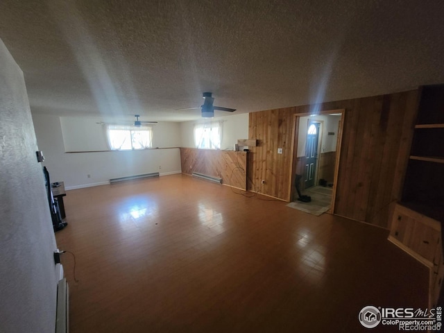 interior space with hardwood / wood-style floors, a baseboard radiator, wooden walls, and ceiling fan