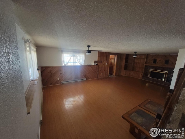 unfurnished living room with hardwood / wood-style floors, a fireplace, wooden walls, baseboard heating, and a textured ceiling