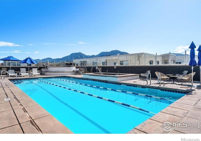 view of pool with a hot tub, a mountain view, and a patio area