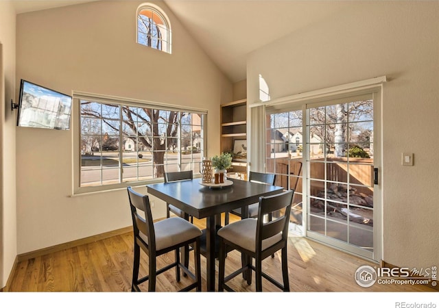 dining space with high vaulted ceiling and light hardwood / wood-style flooring