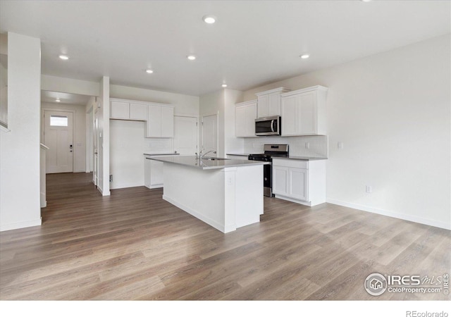 kitchen with white cabinetry, light hardwood / wood-style floors, an island with sink, and appliances with stainless steel finishes