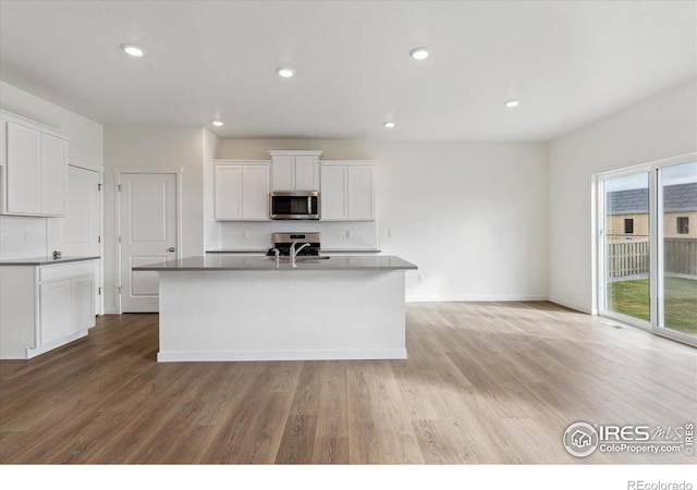 kitchen with sink, tasteful backsplash, stainless steel appliances, a kitchen island with sink, and white cabinets