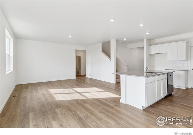 kitchen with sink, white cabinetry, tasteful backsplash, light wood-type flooring, and an island with sink