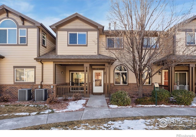 townhome / multi-family property featuring central air condition unit, covered porch, roof with shingles, and brick siding