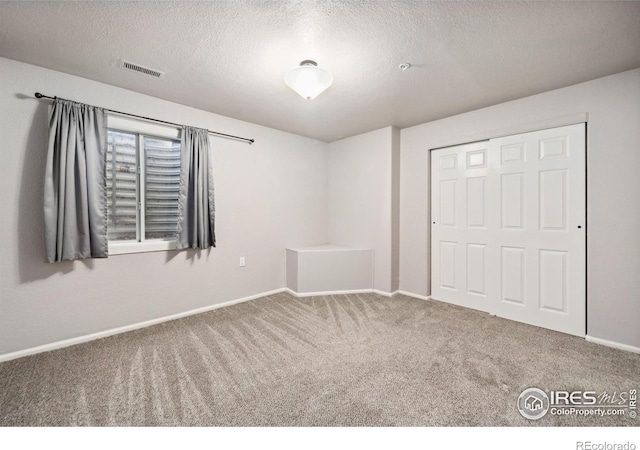 unfurnished bedroom with carpet floors, a closet, visible vents, a textured ceiling, and baseboards