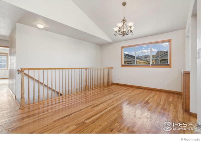 empty room featuring hardwood / wood-style flooring, lofted ceiling, and a chandelier