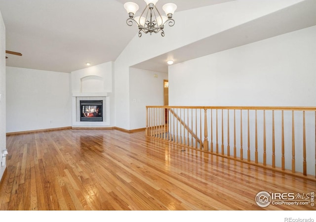 unfurnished living room featuring an inviting chandelier, vaulted ceiling, and light wood-type flooring