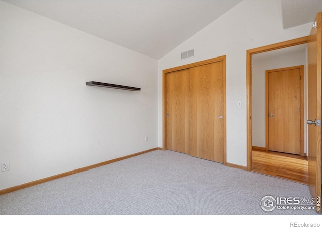 unfurnished bedroom featuring light carpet, vaulted ceiling, and a closet