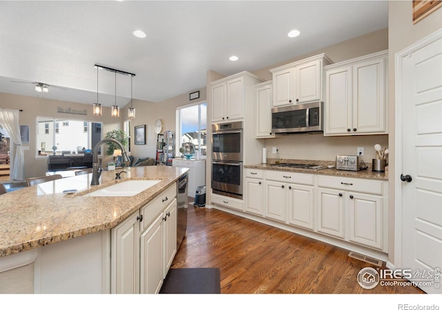 kitchen with decorative light fixtures, stainless steel appliances, wood finished floors, a sink, and light stone countertops