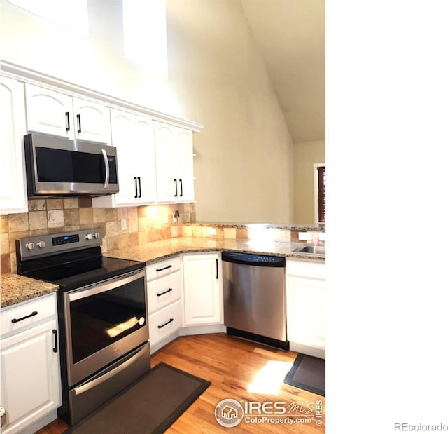 2023 81st Ave, Greeley, CO 80634 - kitchen with appliances with stainless steel finishes, white cabinets, tasteful backsplash, light wood finished floors, and high vaulted ceiling