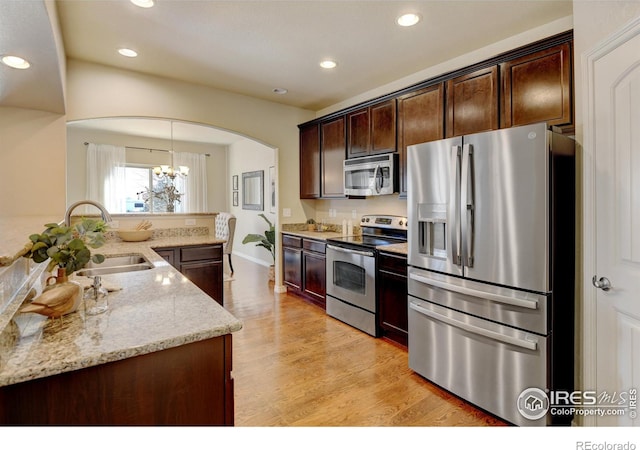 kitchen featuring sink, hanging light fixtures, stainless steel appliances, light stone counters, and light wood-type flooring