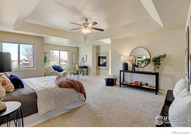 bedroom featuring a tray ceiling, a tiled fireplace, and light carpet