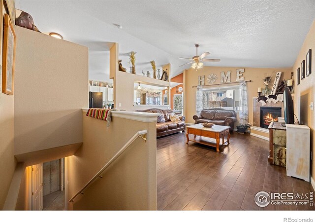 living room featuring dark hardwood / wood-style floors, a fireplace, lofted ceiling, ceiling fan, and a textured ceiling