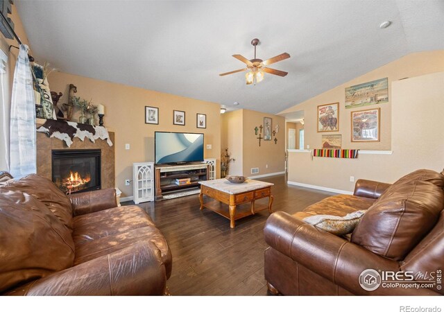 living room with a tiled fireplace, lofted ceiling, dark wood-type flooring, and ceiling fan