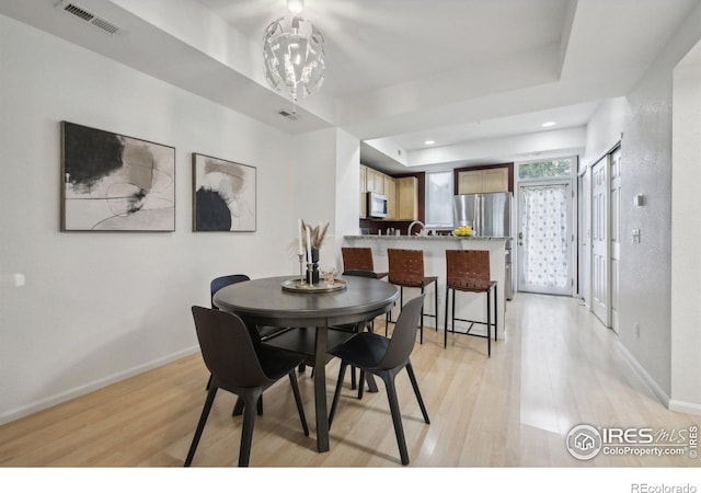 dining room featuring an inviting chandelier, a raised ceiling, and light wood-type flooring