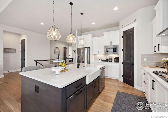 kitchen with appliances with stainless steel finishes, pendant lighting, sink, white cabinets, and a center island with sink