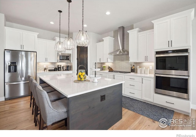 kitchen with white cabinetry, stainless steel appliances, an island with sink, and wall chimney exhaust hood