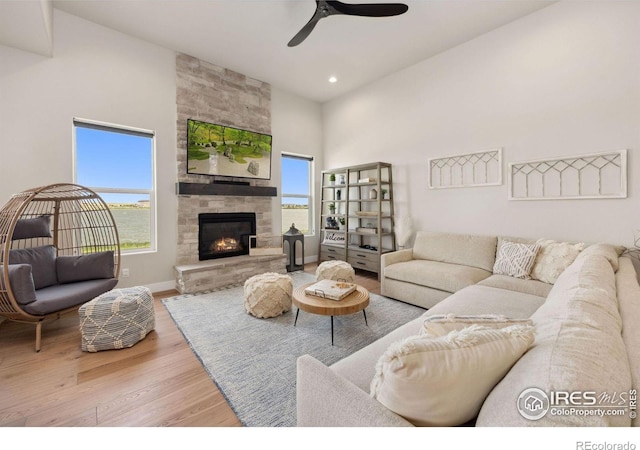 living room with a stone fireplace, plenty of natural light, light hardwood / wood-style floors, and a high ceiling