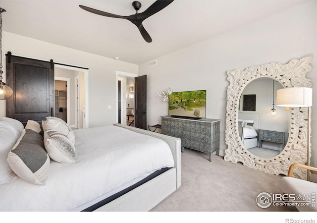 carpeted bedroom featuring a barn door, a spacious closet, and ceiling fan