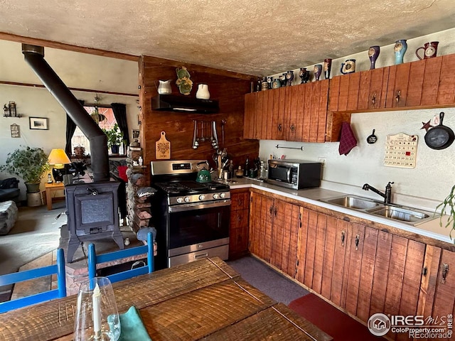 kitchen with appliances with stainless steel finishes, sink, a textured ceiling, and a wood stove