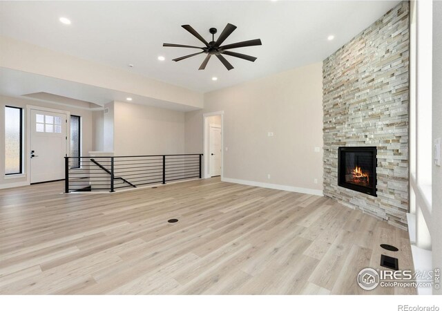 unfurnished living room with ceiling fan, a stone fireplace, and light hardwood / wood-style floors