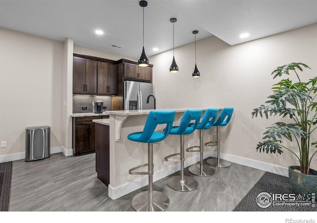 kitchen with dark brown cabinets, stainless steel fridge, decorative light fixtures, and a kitchen breakfast bar