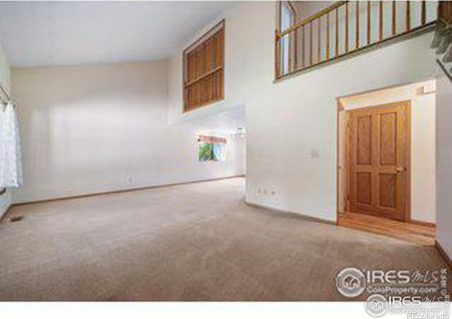 unfurnished living room featuring carpet and a high ceiling