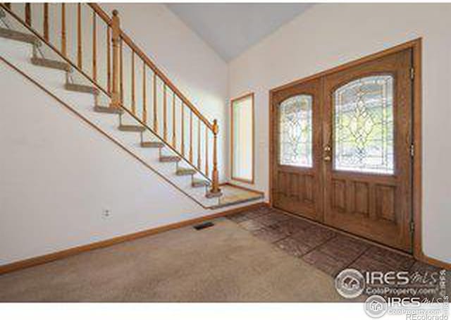 foyer featuring french doors, lofted ceiling, and carpet