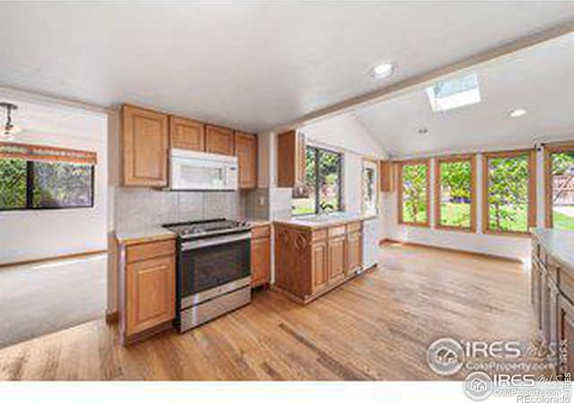 kitchen with tasteful backsplash, vaulted ceiling, gas stove, and light wood-type flooring