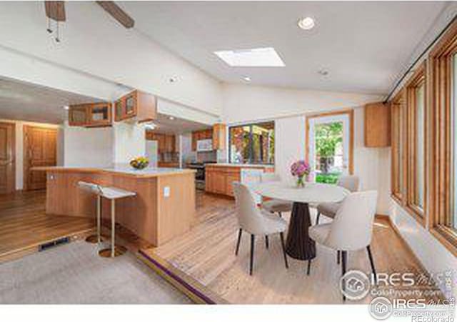 dining area with vaulted ceiling with skylight and light wood-type flooring