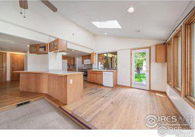 kitchen with vaulted ceiling with skylight, kitchen peninsula, and light hardwood / wood-style floors