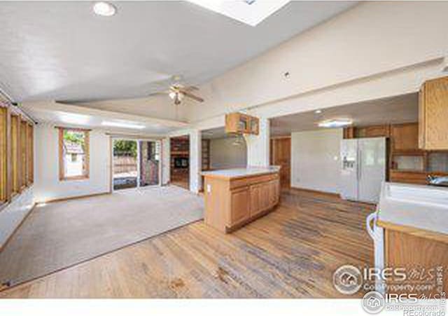 kitchen with lofted ceiling with skylight, sink, hardwood / wood-style flooring, white refrigerator with ice dispenser, and ceiling fan