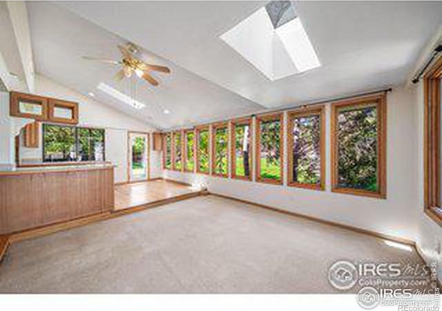 unfurnished living room with ceiling fan, lofted ceiling with skylight, and carpet