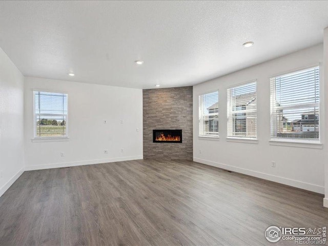 unfurnished living room featuring plenty of natural light, wood finished floors, a large fireplace, baseboards, and recessed lighting