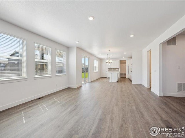 unfurnished living room featuring a chandelier, light wood-style floors, recessed lighting, and baseboards