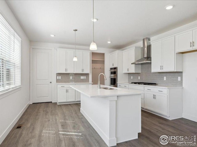 kitchen with wall chimney exhaust hood, stainless steel double oven, a sink, gas cooktop, and dark wood-type flooring